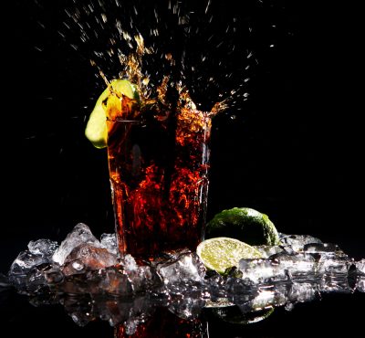 Fresh cola drink with splashes of water and green lime on black background